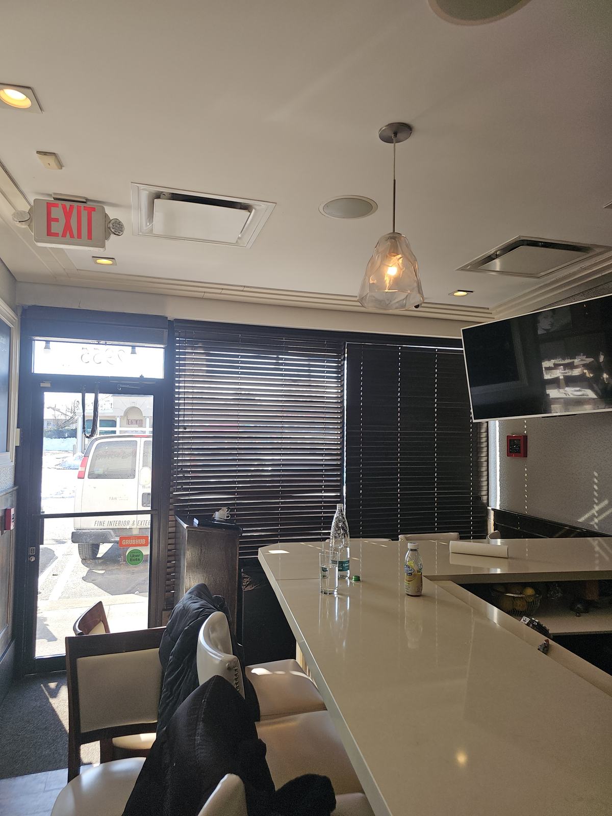 Dark woven shade lowered over the entrance glazing of a restaurant, seen from the bar inside