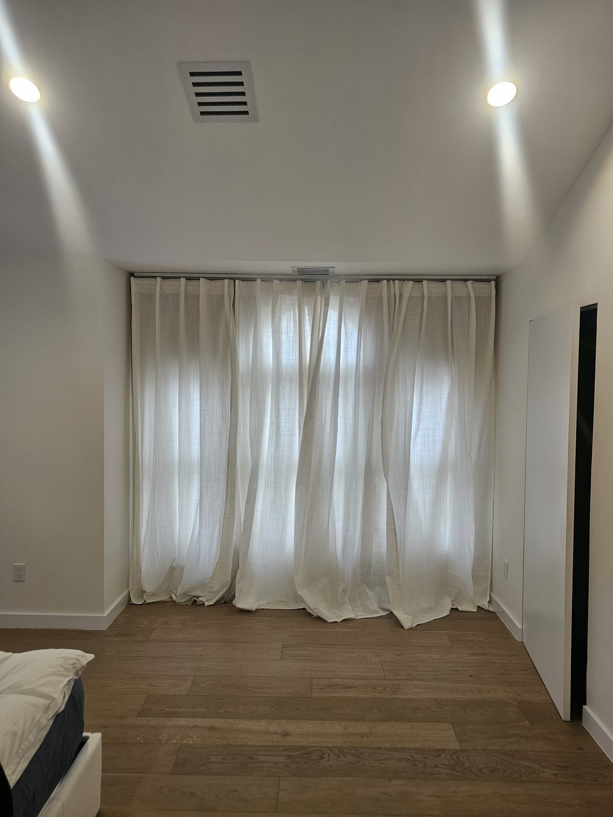 Floor-length sheer drapery panels hung high and wide across a bedroom window